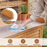 A stainless steel outdoor countertop with a wooden cabinet base, shown in a real patio setting with a person wiping the surface with a blue cloth. The image includes text overlays reading 'Premium Stainless Steel Tabletop,' 'Anti-fall Baffles,' and feature icons for 'Rust-free,' 'Easy-to-clean,' and 'Waterproof.