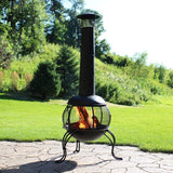 Black metal chiminea with flames on a stone patio in a garden setting
