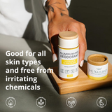 Hand holding a container of aluminum-free deodorant with product details and benefits on a wooden board.