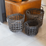 Three woven baskets on a tiled floor with a brown leather chair in the background.