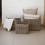 Three woven baskets with a towel and pillows on a tiled floor against a white brick wall.