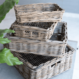 Stack of wicker baskets on a light surface with a plant in the corner