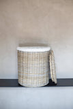 Wicker laundry basket with a white liner on a gray surface against a beige wall.