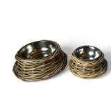 Two round pet bowls, one larger and one smaller, featuring a natural woven rattan exterior and a polished stainless steel interior, set against a plain white background.