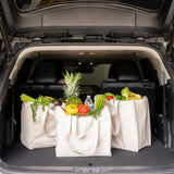 Trunk of a car with three reusable grocery bags filled with fresh produce.