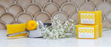 Yellow soap bars and packaging with 'Good Life' branding on a tiled wall background.