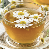 Glass cup of chamomile tea with flowers on a wooden surface