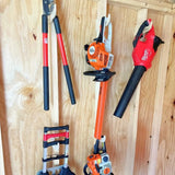 Gardening tools including a hedge trimmer, pruner, and leaf blower mounted on a wooden wall.