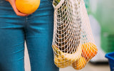 Person holding a mesh bag with oranges and an orange in their hand.
