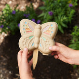 Butterfly-shaped Curious Critters Garden Kits held by two hands with a garden background