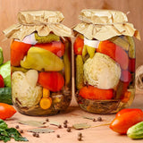Two jars of pickled vegetables on a wooden surface with a brown background