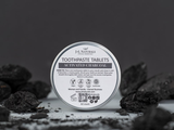 Container of H.H. Naturals toothpaste tablets with activated charcoal on a dark background