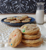 Stack of cookies with colorful candies on a plate, next to a bottle of milk against a chalkboard background.