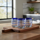 Three glass tumblers with blue stripes on a wooden cutting board in a kitchen setting.