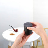 Person holding a black grinder with a small pipe and tobacco on a white table.