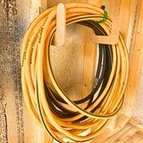 Coiled yellow garden hose hanging on a wooden hook against a wooden wall.