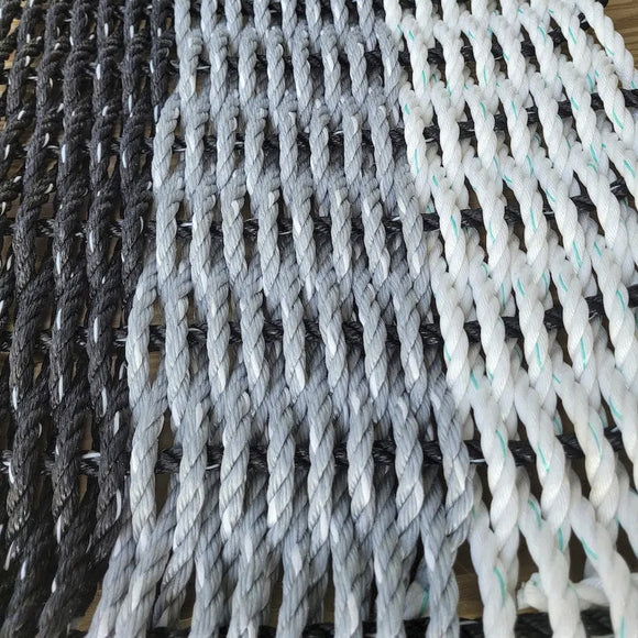 Three ropes of different colors (black, gray, white) on a wooden surface.