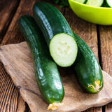Three Organic Heirloom Poinsett 76 Cucumbers on a wooden cutting board with one sliced, on a rustic wooden table.