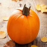Heirloom Organic Small Sugar Pumpkin with a stem on a wooden surface with autumn leaves