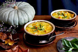 Two bowls of pumpkin soup with a RARE Organic Heirloom Jarrahdale Pumpkin and autumn leaves on a wooden table.