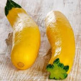 Two Heirloom Organic Early Prolific Straight neck Squash Seeds with green stems on a wooden surface