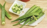 Organic Heirloom Emerald Okra on a wooden cutting board with a small bowl of okra pieces.