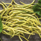 Heirloom Organic Yellow Pencil Pod Bush Beans with green leaves on a wooden surface