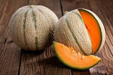 Heirloom organic Delicious 51 Cantaloupe on a wooden surface, one whole and one sliced open.