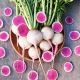 Asian Heirloom Organic Watermelon Radishes with pinkish-purple skin on a wooden plate, surrounded by additional radishes on a gray background.