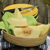 Rare Heirloom Organic Sharlyn Melon Seeds (Aka Pineapple Melon, Ananas Melon, Ananas D'Amerique a Chair Verte) in a woven basket with a green cloth and knife on a wooden surface.