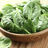 Wooden bowl filled with Heirloom Organic Whale Spinach on a wooden surface