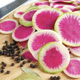 Asian Heirloom Organic Watermelon Radishes on a wooden cutting board with black peppercorns and bay leaves.
