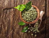 Green coffee beans in a wooden bowl with leaves on a rustic wooden background