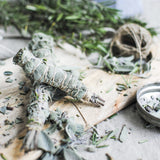Sage smudge sticks on a wooden board with greenery and a candle in the background