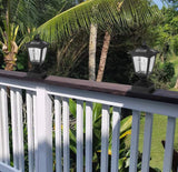 Two outdoor lights on a railing with palm trees and greenery in the background