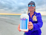 Person holding a bottle of 'Sea Salt' lotion on a beach