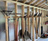 Gardening tools including shovels and a rake hanging on a wooden wall.