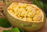 Jackfruit cut open with visible flesh, surrounded by green leaves, on a wooden surface.