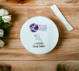Lavender body butter container on a wooden surface with flowers and a bar of soap.