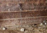 Leaf Wrap Fire Poker leaning against a wooden wall with a natural ground below