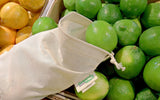 Green limes in a cloth bag with an 'Organic' label, surrounded by oranges.