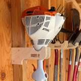 Stihl hedge trimmer hanging on a wooden wall with gardening tools.