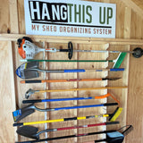 Set of gardening tools hanging on a wooden panel with 'Hang This Up' sign above.