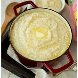 Red pot filled with creamy grits with a pat of butter on top, surrounded by kitchen utensils.