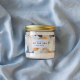 Jar of bath salts labeled 'Of the Sea' on a textured gray fabric background
