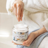 Person holding a jar of 'Of the Sea' bath salts with a spoonful being scooped out.