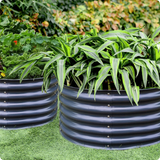 Two black corrugated planters with green plants on a grassy background