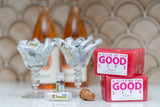 Two 'A Slice of the Good Life' soap bars on a table with drinks and a cork in the background.