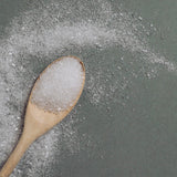 Wooden spoon filled with white granulated Revive Bath Salts  on a gray surface