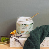 Jar of bath salts labeled 'Revive' with a green towel and lavender on a neutral background